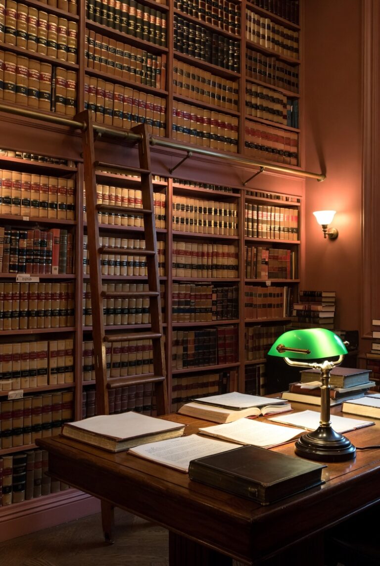 Traditional law library with floor-to-ceiling legal books, rolling ladder, and green banker's lamp on a wooden desk
