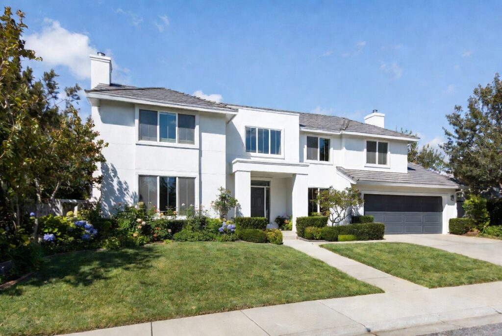 Two-storey white stucco luxury home with manicured front lawn, hydrangeas, trimmed hedges, and a double grey garage door on a sunny day
